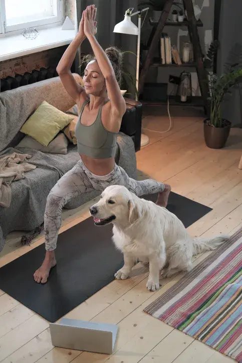 Une femme en posture de yoga chez elle, un chien golden assis à ses côtés