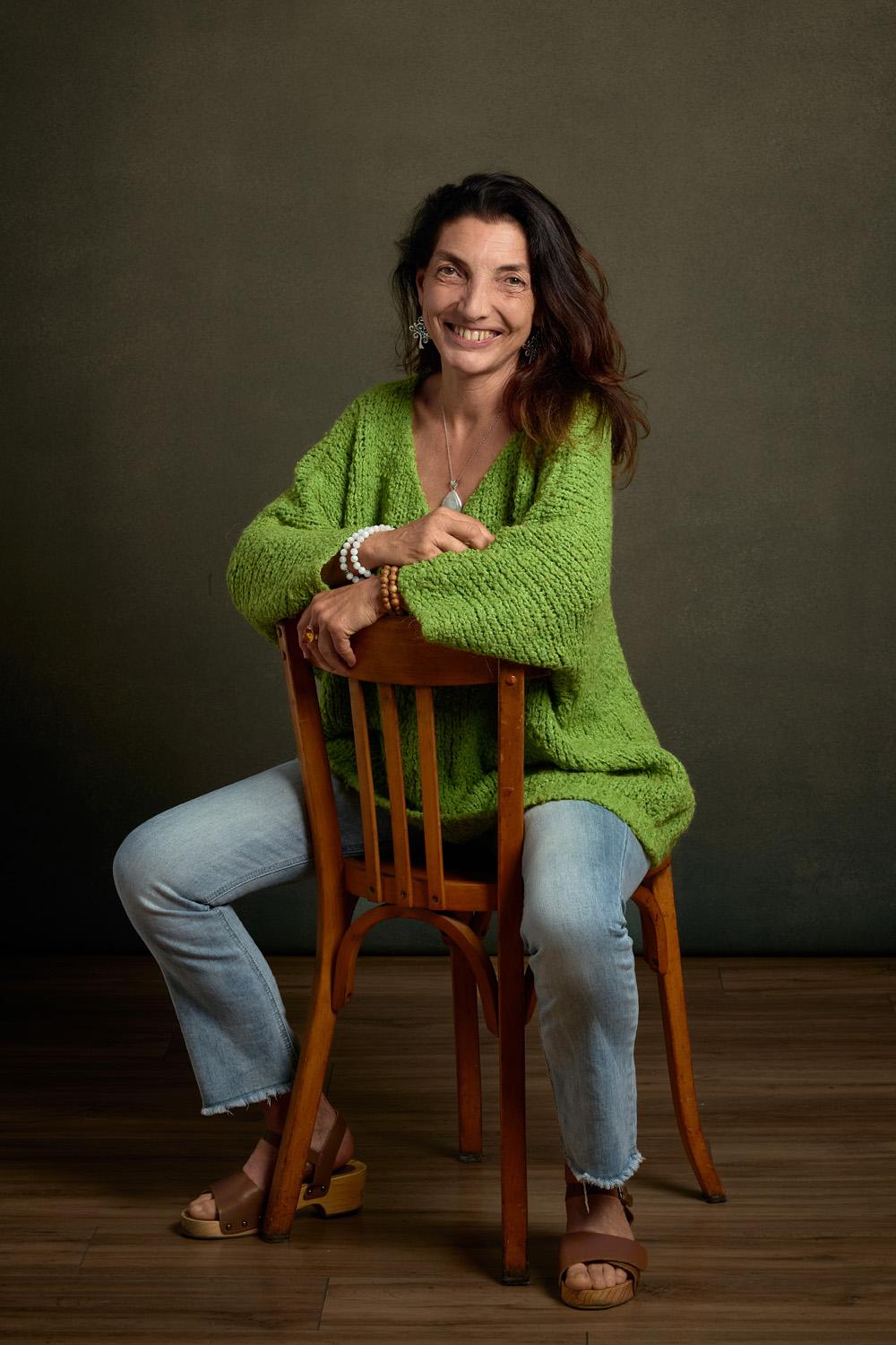 Frédérique Wurfel, souriante, assise sur une chaise en bois, portant un pull vert